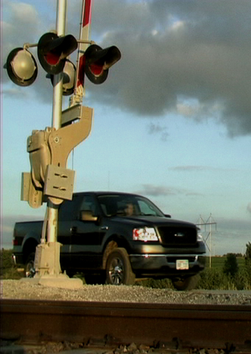 A railroad CEO conducts a sensitive business negotiation parked on a live railroad crossing in the Nebraska segment of We Pedal Uphill: Stories from the States, 2001-2008.